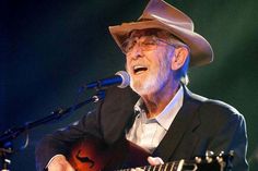 an older man wearing a suit and hat singing into a microphone while holding a guitar