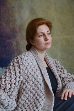 a woman sitting on a couch wearing a knitted cardigan and looking off into the distance