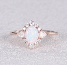 a white opal and diamond ring on top of a gray surface with small diamonds around it