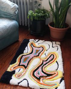 a rug on the floor in front of a couch and potted plant next to it