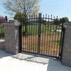 an iron gate and brick wall in front of a grassy area