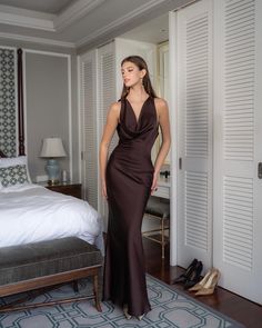 a woman standing in front of a bed wearing a brown dress