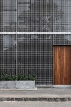 two planters on the sidewalk in front of a building with metal mesh walls and wooden doors