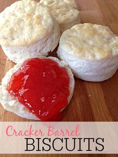 three biscuits with jam on them sitting on a wooden table next to another biscuit