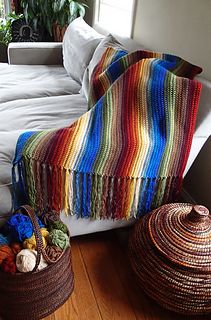 two baskets are sitting on the floor next to a couch with a multicolored blanket