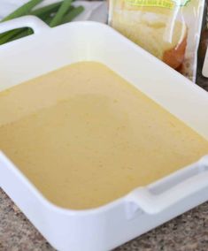 a white dish filled with sauce next to some green onions and seasoning on the counter