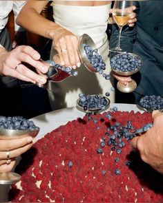 several people are pouring blueberries into small bowls on a table with wine glasses in front of them