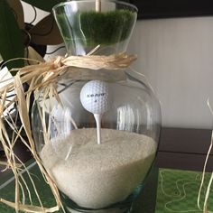 a golf ball in a glass vase filled with sand and grass on top of a table