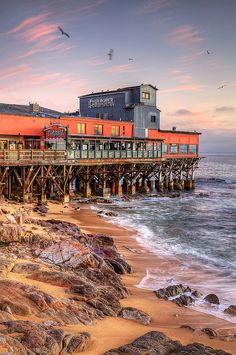 an old pier on the beach with birds flying over it