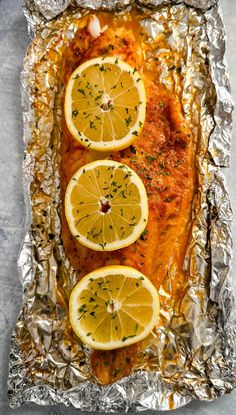 fish covered in lemons and herbs on foil with some seasoning sprigs