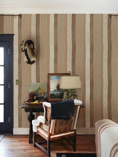 a living room with striped wallpaper and a chair in front of a table that has an animal head mounted on the wall