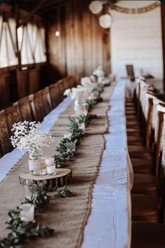 a long table with candles and greenery on it in front of a wooden wall