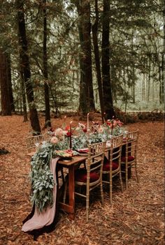 a table set up in the woods with candles and flowers on it for an outdoor dinner