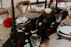 the table is set with black and white plates, silverware, and red roses