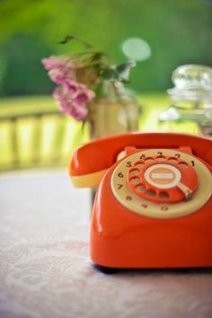 an orange phone sitting on top of a table next to a vase filled with flowers