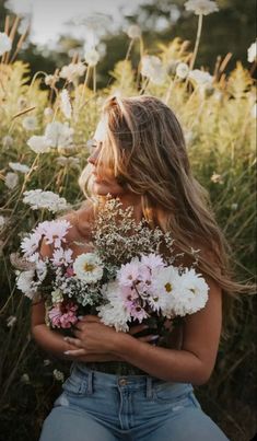 a woman sitting in a field with flowers on her chest and arms around her body