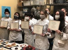 some people in white coats and masks holding up diplomas next to plates with pastries on them