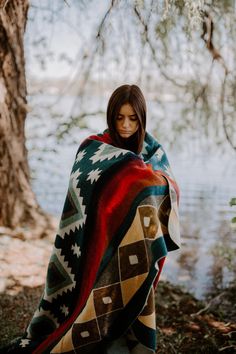 a doll is wrapped up in a blanket by the water's edge with a tree behind it