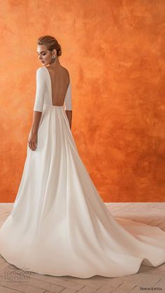 a woman in a white wedding dress standing against an orange wall with her back to the camera