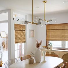 a dining room table with chairs and a vase on top of it in front of two windows