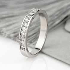 a white gold wedding ring with diamonds on it's side, sitting next to a piece of fabric