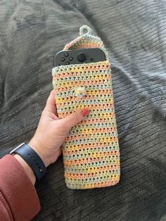 a hand holding an iphone case made out of crocheted material on top of a bed