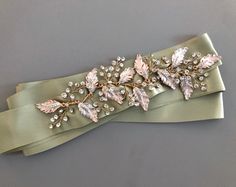 a green satin ribbon with leaves and crystals on the edge is laying on a gray surface