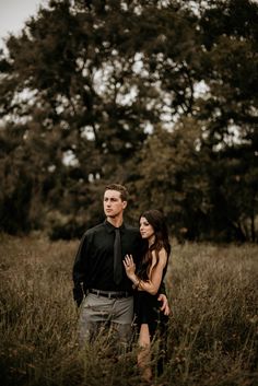 a young man and woman standing in tall grass with trees in the backgroud