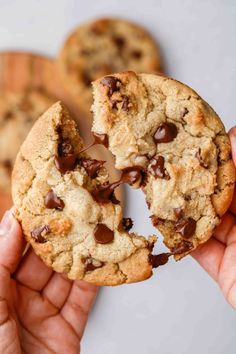 someone is holding a chocolate chip cookie in their hand and it has one bite taken out