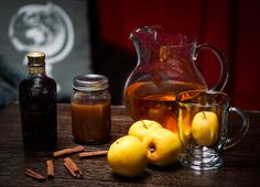 apples and cinnamons sit on a wooden table next to a pitcher of apple cider