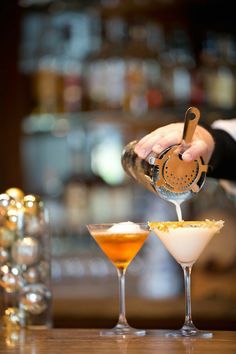 a bartender pours drinks into martini glasses