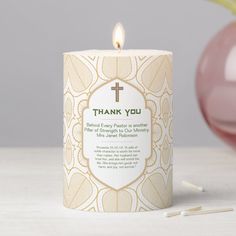 a candle with a cross on it sitting next to a pink vase and some matches