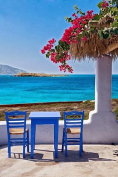 two blue chairs sitting at a table near the ocean