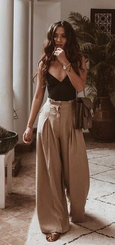 a woman standing in front of a potted plant wearing wide legged pants and a black top