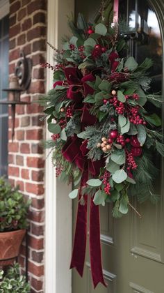 a wreath hanging on the front door of a house with greenery and red berries