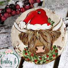 a wooden ornament with a painting of a cow wearing a santa claus hat