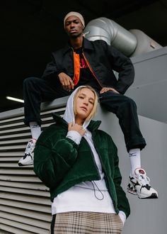 two people standing next to each other in front of a building and one is wearing a green jacket