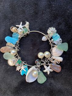 "Kingman Turquoise Ocean Jasper Sea shells beach glass Pearls and Sterling plated beach charms on a bangle charm bracelet. With Ocean Jasper, 6 Pearls, 2 Sea shells, 6 pieces of beach glass, 12 beach charms, 3 hand blown glass beads, 1 Petoskey stone, a piece of Kingman Turquoise and 2 blue glass beads finish this bangle charm bracelet.   The bangle bracelet is  2.5\" inches in width. See all my charm bracelets here: https://www.etsy.com/shop/MoonwaterJewelryShop?section_id=34394213 All my bracelets are different and would be considered one of a kind. View my collection of Kingman Arizona Turquoise here: https://www.etsy.com/shop/MoonwaterJewelryShop?section_id=28192591  I've been selling on eBay since 2003 Came to Etsy to sell jewelry. Returns and exchange details ► RETURNS / EXCHANGES Al Shell Charm Bracelet, Beach Glass Nails, Sea Glass Bangle, Beach Charms Bracelet Jewelry, Bohemian Beach Bracelets With Charms, Bohemian Charm Bracelets For The Beach, Beach Ocean-inspired Charm Bracelet, Handmade Charm Bangle For Beach, Handmade Dangle Bracelets For Beach