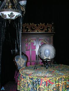 an old fashioned table and chair in a room with dark walls, black curtains, and a fancy chandelier hanging from the ceiling