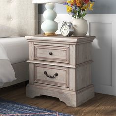 a nightstand with two drawers and a clock on it next to a bed in a bedroom