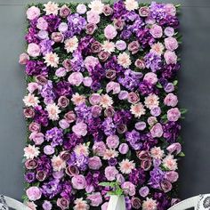 purple and white flowers are growing on the side of a wall in front of a chair