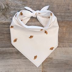 a white bandana with brown leaves on it and a knot at the top is laying on a wooden surface