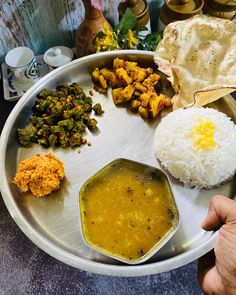 a plate with rice, curry and other food items on it is shown in front of a person's hand