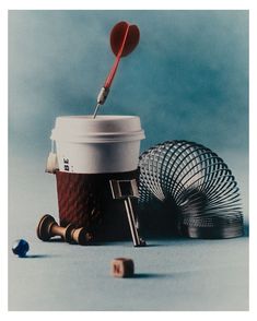 a coffee cup with a red spoon sticking out of it next to other cups and objects