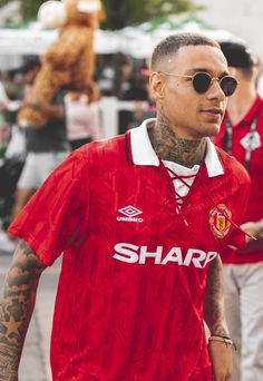 a man in a red shirt and sunglasses walking down the street with other people behind him