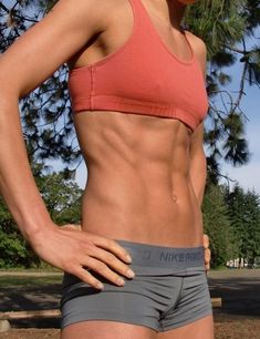 a woman in a red sports bra top and gray shorts with her hands on her hips