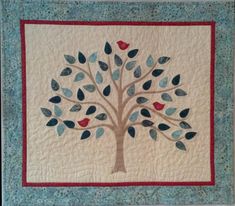 a quilted wall hanging with a tree on it's side and birds perched on the leaves