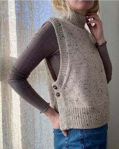 a woman standing in front of a window with her hands on her hips wearing a sweater and jeans