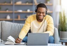 a man sitting at a table with a laptop computer and headphones on, smiling