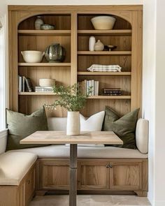 a wooden table sitting under a window next to a shelf filled with books and vases